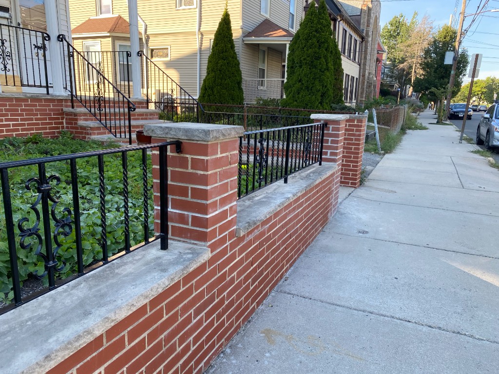 Ornamental black iron fence on brick wall with stone caps — residential Massachusetts frontage