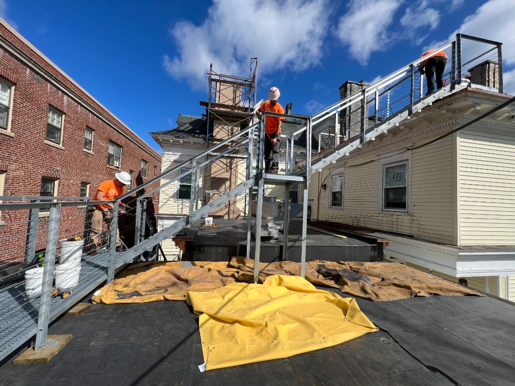 Irias crew installing galvanized steel rooftop access stair with open grating treads and cable railings — Greater Boston